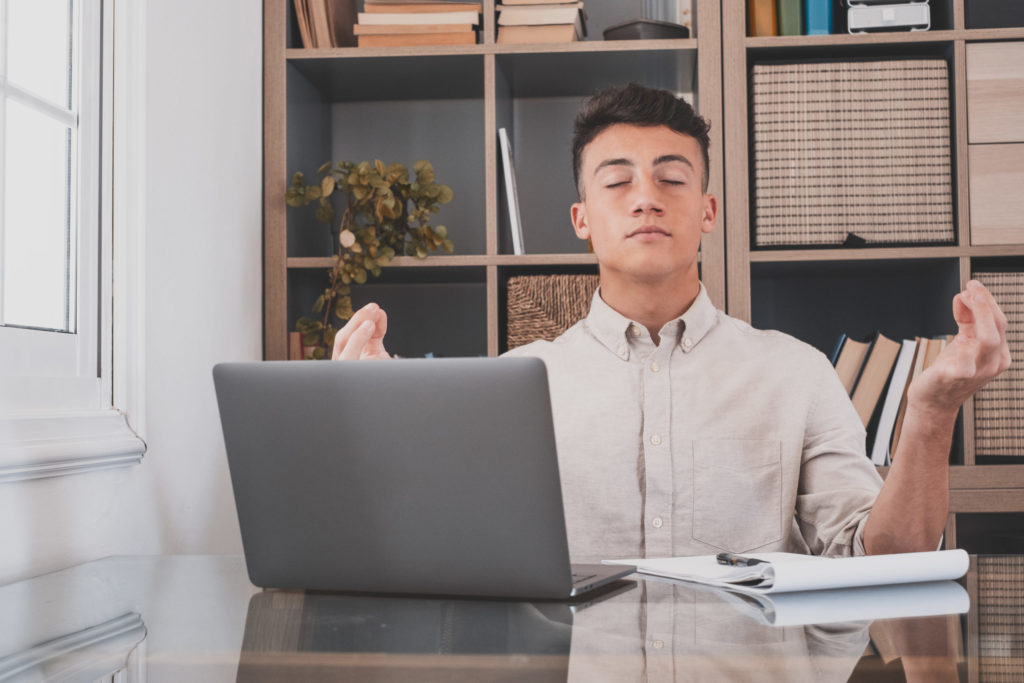 Serene office male teenager sit at desk relaxing doing yoga